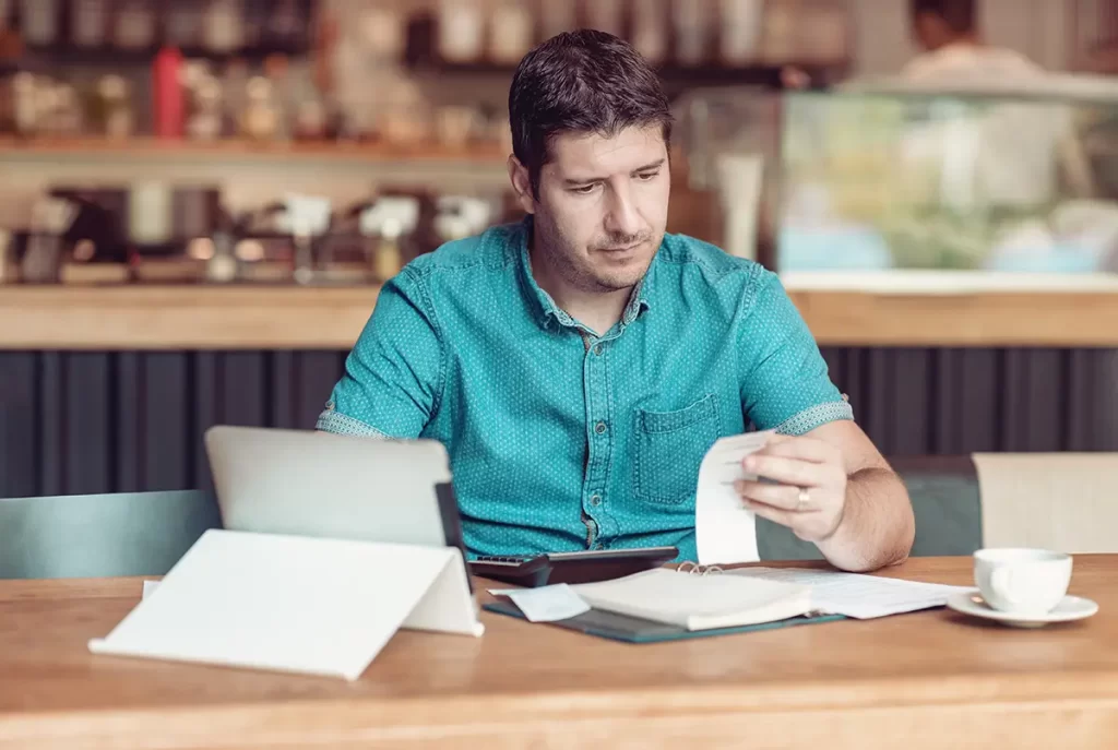 A man with an ipad and receipts looking stressed