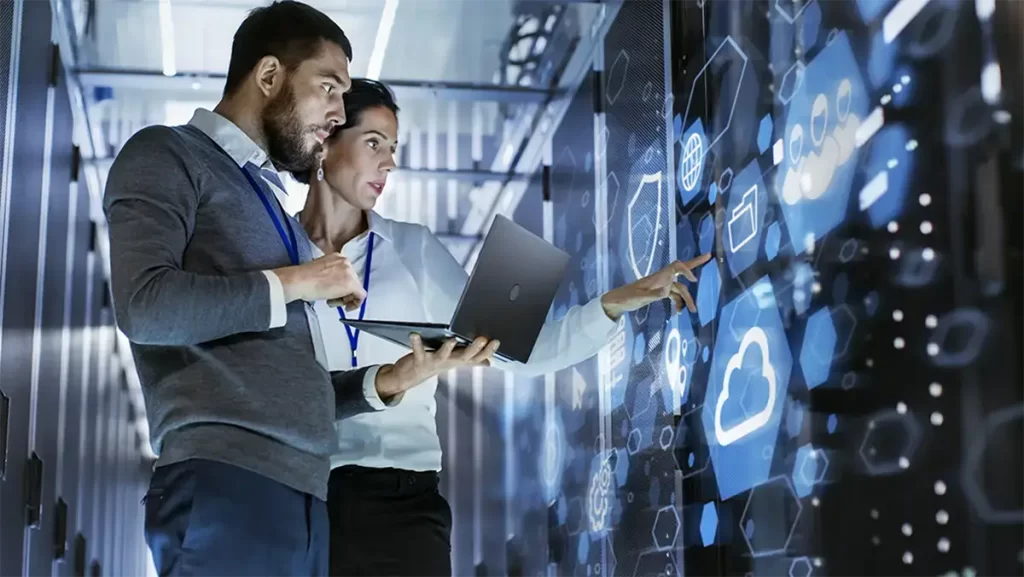 A man holding a laptop while a woman points at a digital screen with a folder icon