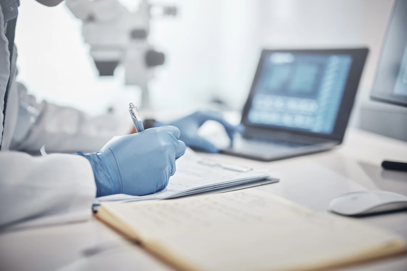 A medical professional with blue gloves on looking at a computer and writing in a notebook