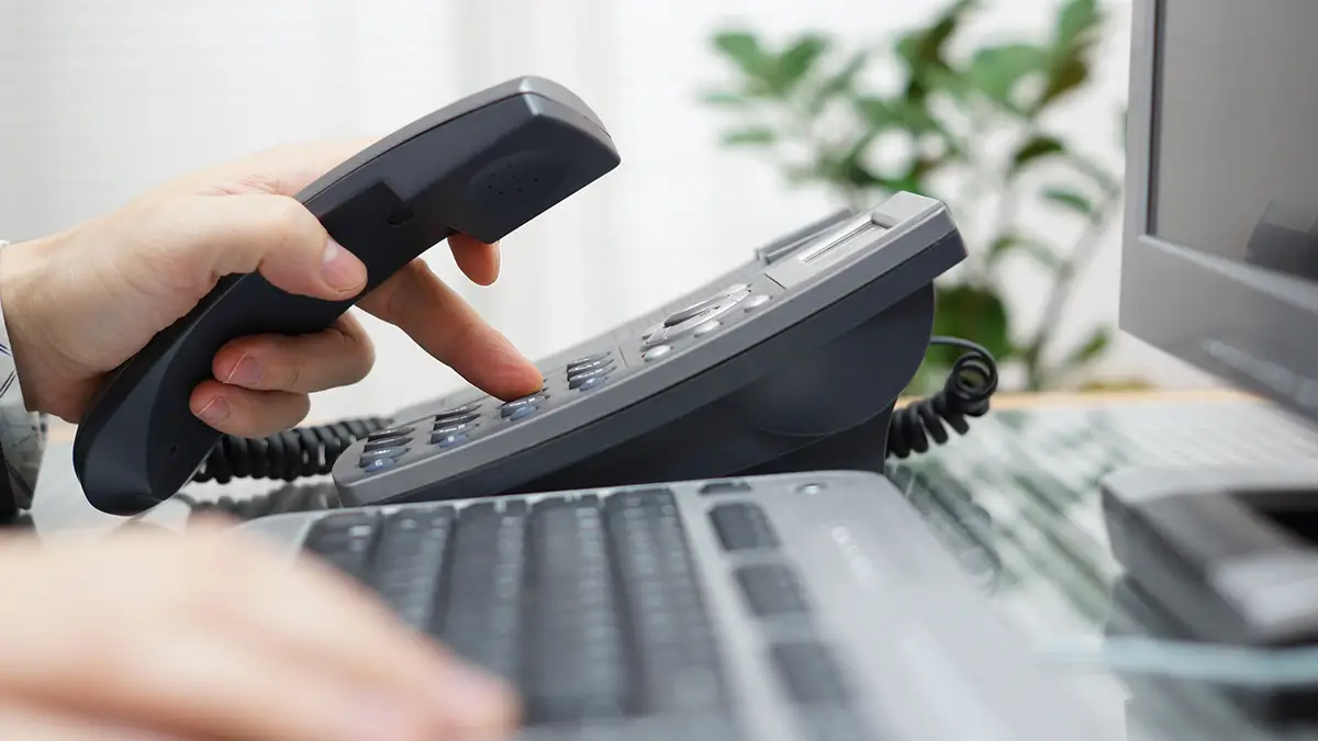 An office worker at the computer dialing on the desk phone, representing voip solutions